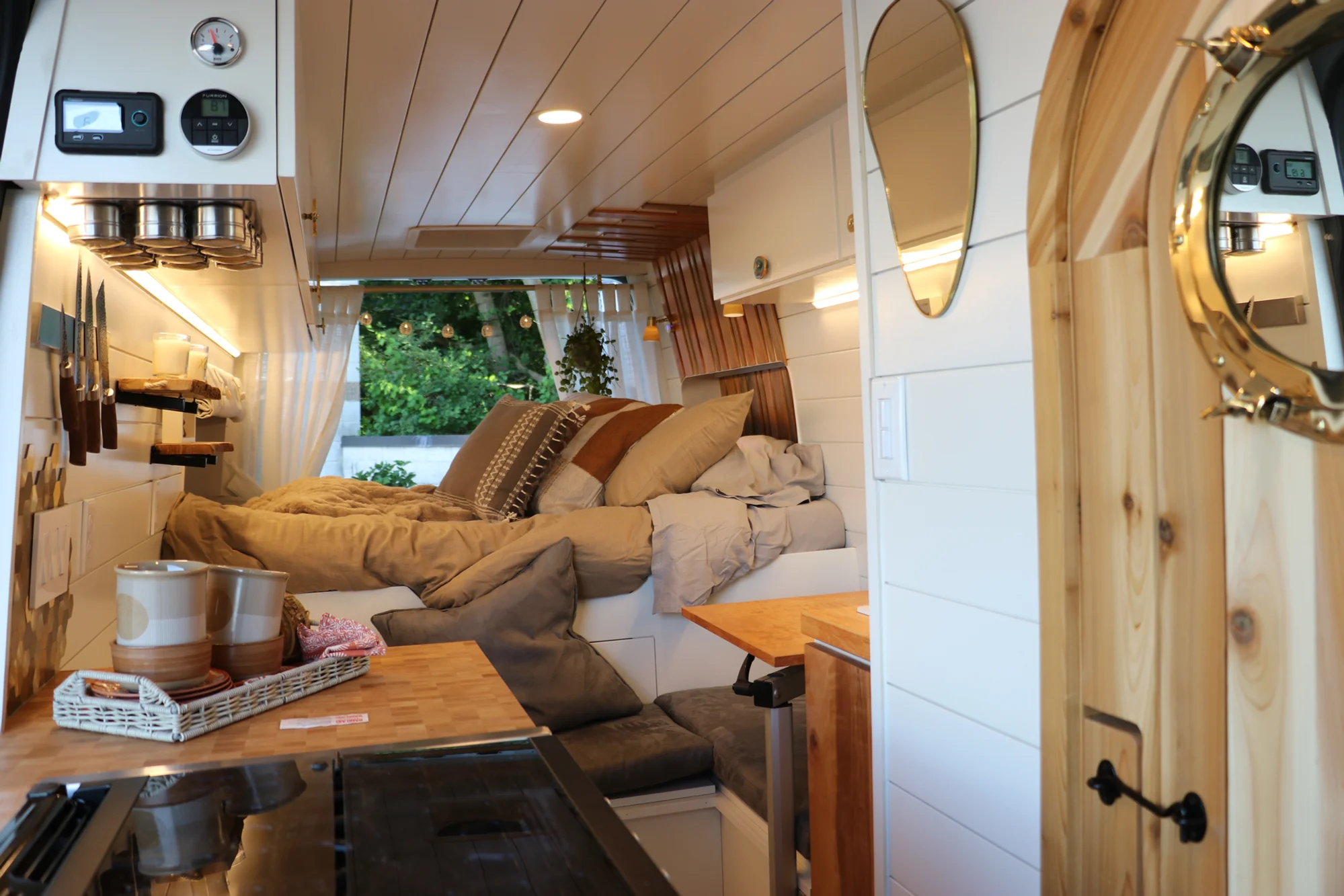 The Drifter 101 custom Ford Transit campervan built for Nikki and Rocco by Drifter Vans, boho interior with an arched wood shower door, gold details, string lights, and hanging plants