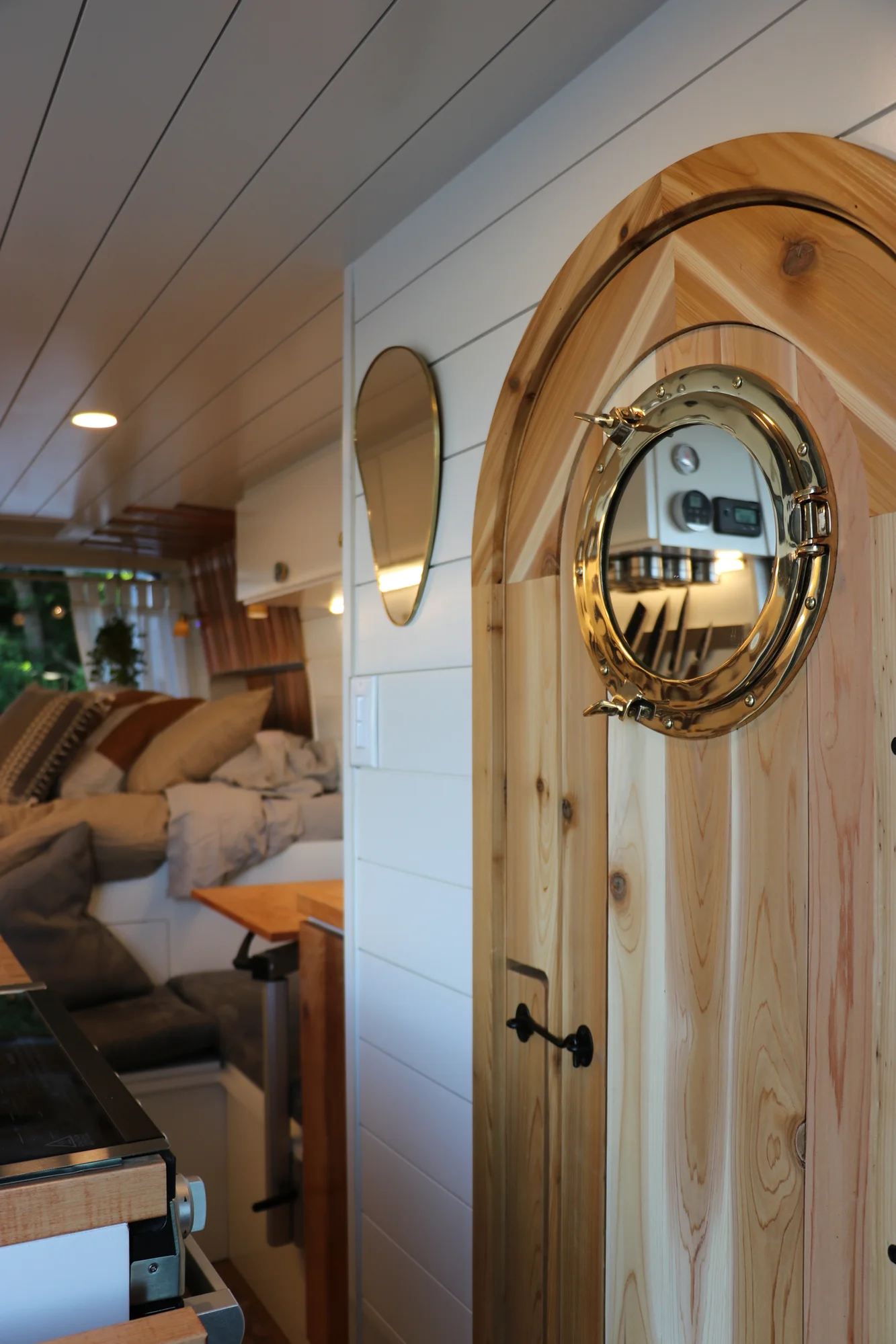 The Drifter 101 custom Ford Transit campervan built for Nikki and Rocco by Drifter Vans, boho interior with an arched wood shower door, gold details, string lights, and hanging plants