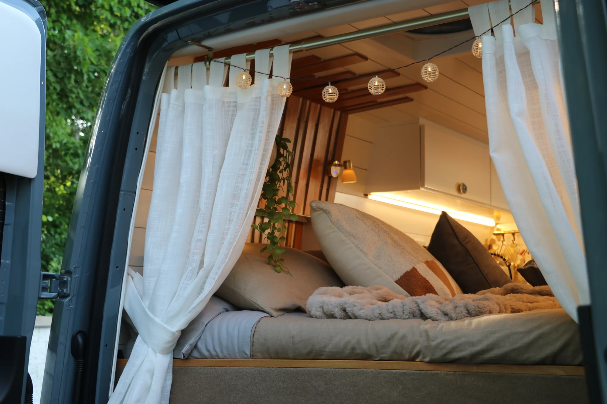 The Drifter 101 custom Ford Transit campervan built for Nikki and Rocco by Drifter Vans, boho interior with an arched wood shower door, gold details, string lights, and hanging plants