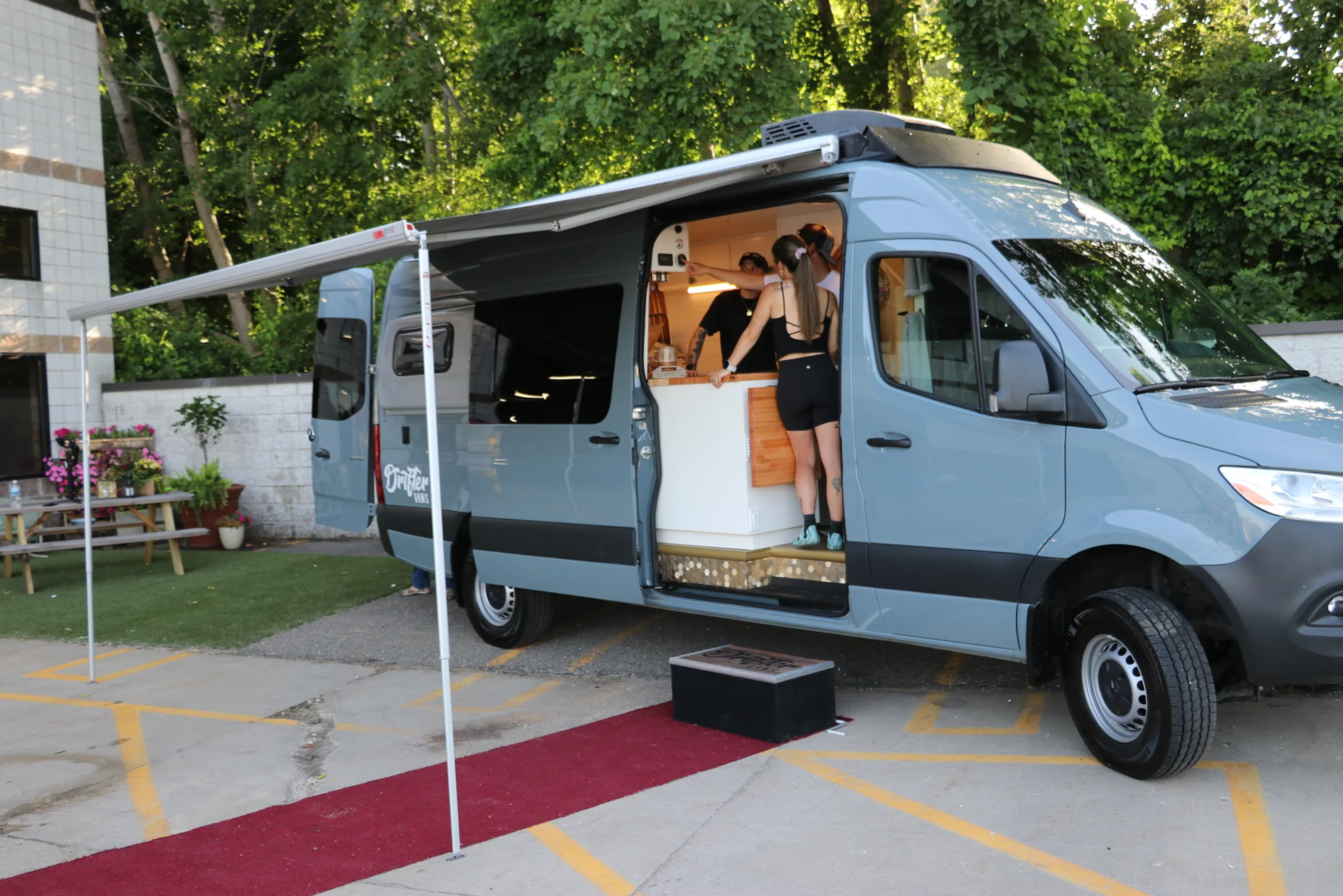The Drifter 101 custom Ford Transit campervan built for Nikki and Rocco by Drifter Vans, boho interior with an arched wood shower door, gold details, string lights, and hanging plants