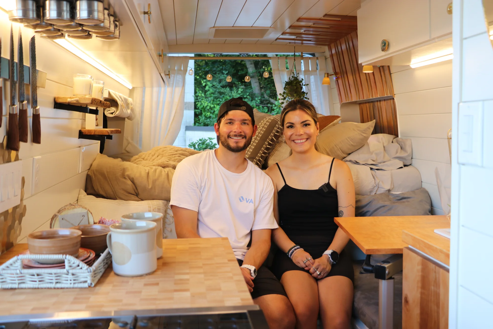 The Drifter 101 custom Ford Transit campervan built for Nikki and Rocco by Drifter Vans, boho interior with an arched wood shower door, gold details, string lights, and hanging plants