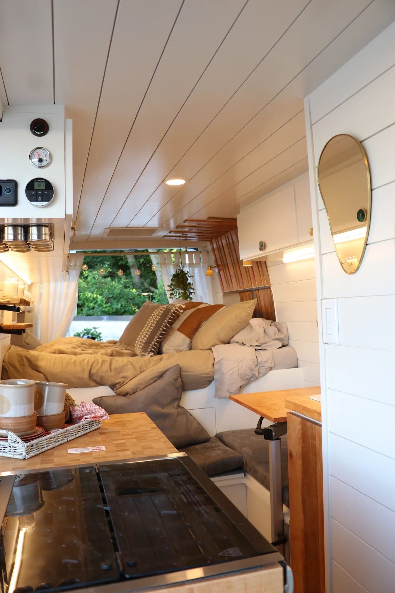 The Drifter 101 custom Ford Transit campervan built for Nikki and Rocco by Drifter Vans, boho interior with an arched wood shower door, gold details, string lights, and hanging plants