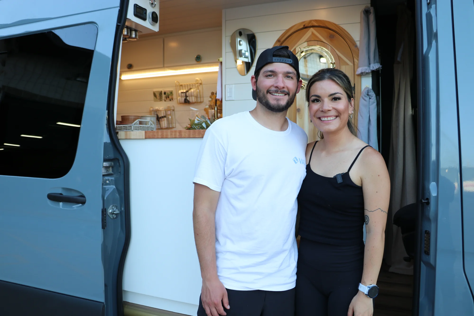 The Drifter 101 custom Ford Transit campervan built for Nikki and Rocco by Drifter Vans, boho interior with an arched wood shower door, gold details, string lights, and hanging plants