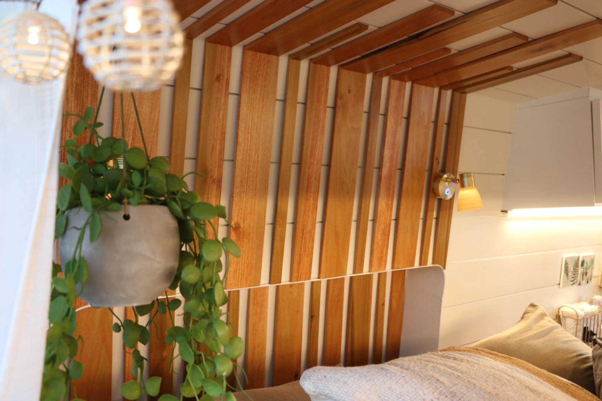 The Drifter 101 custom Ford Transit campervan built for Nikki and Rocco by Drifter Vans, boho interior with an arched wood shower door, gold details, string lights, and hanging plants