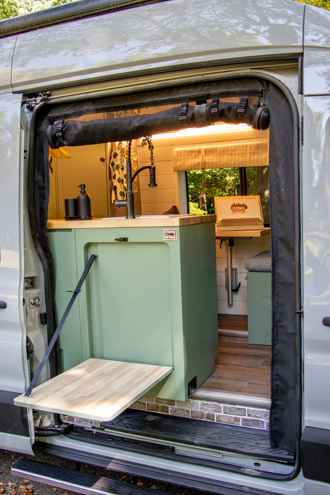The Drifter 101 custom Ford Transit campervan built for Steph and Jen by Drifter Vans, Wanderer layout with a brick backsplash, sage green cabinetry, and farmhouse lighting