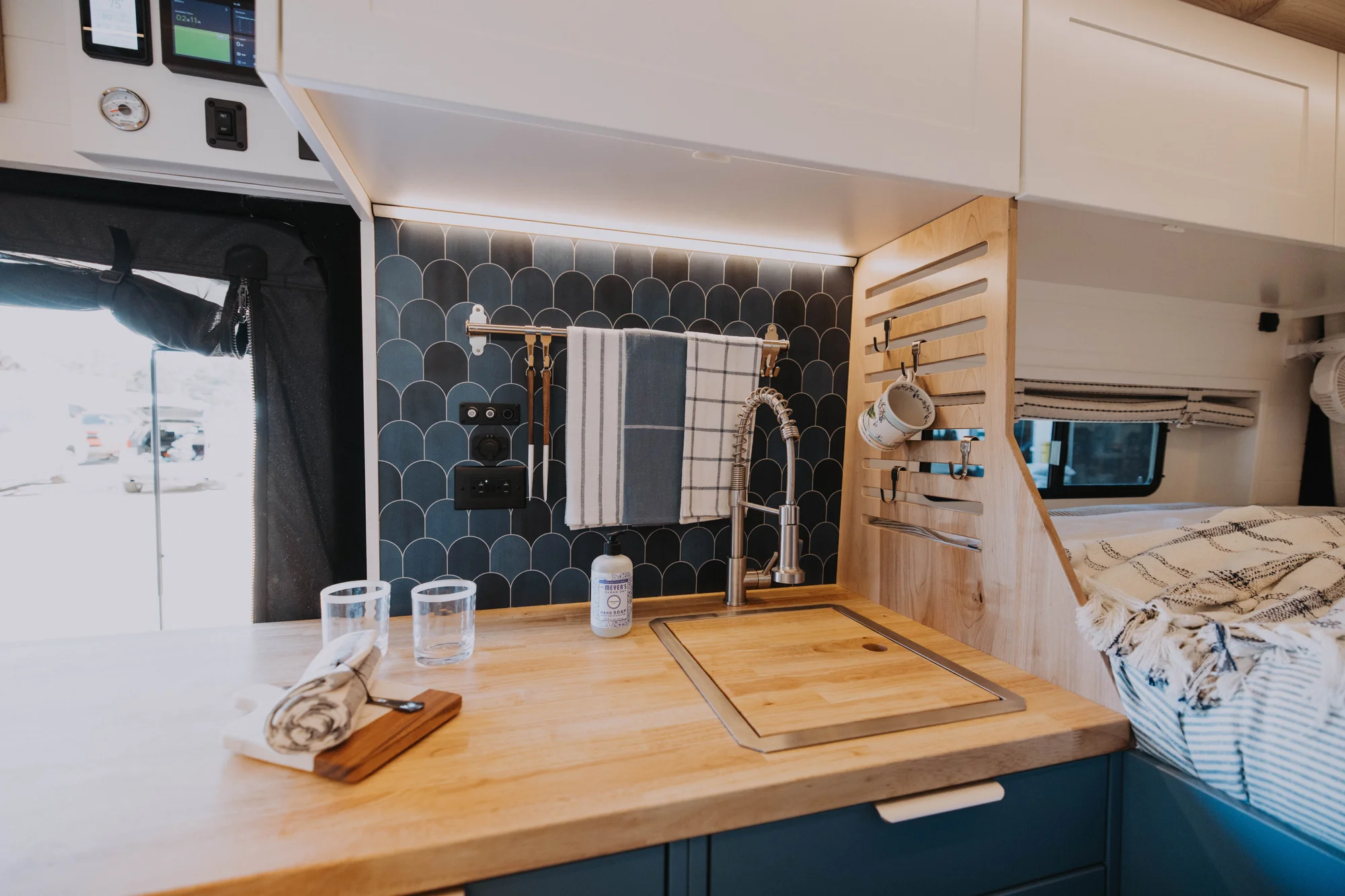 The Drifter 101 custom Ford Transit campervan built for Ayala by Drifter Vans, Drifter layout with warm wood cabinetry, a blue backsplash, flip-down shower, and an Avalanche Grey exterior