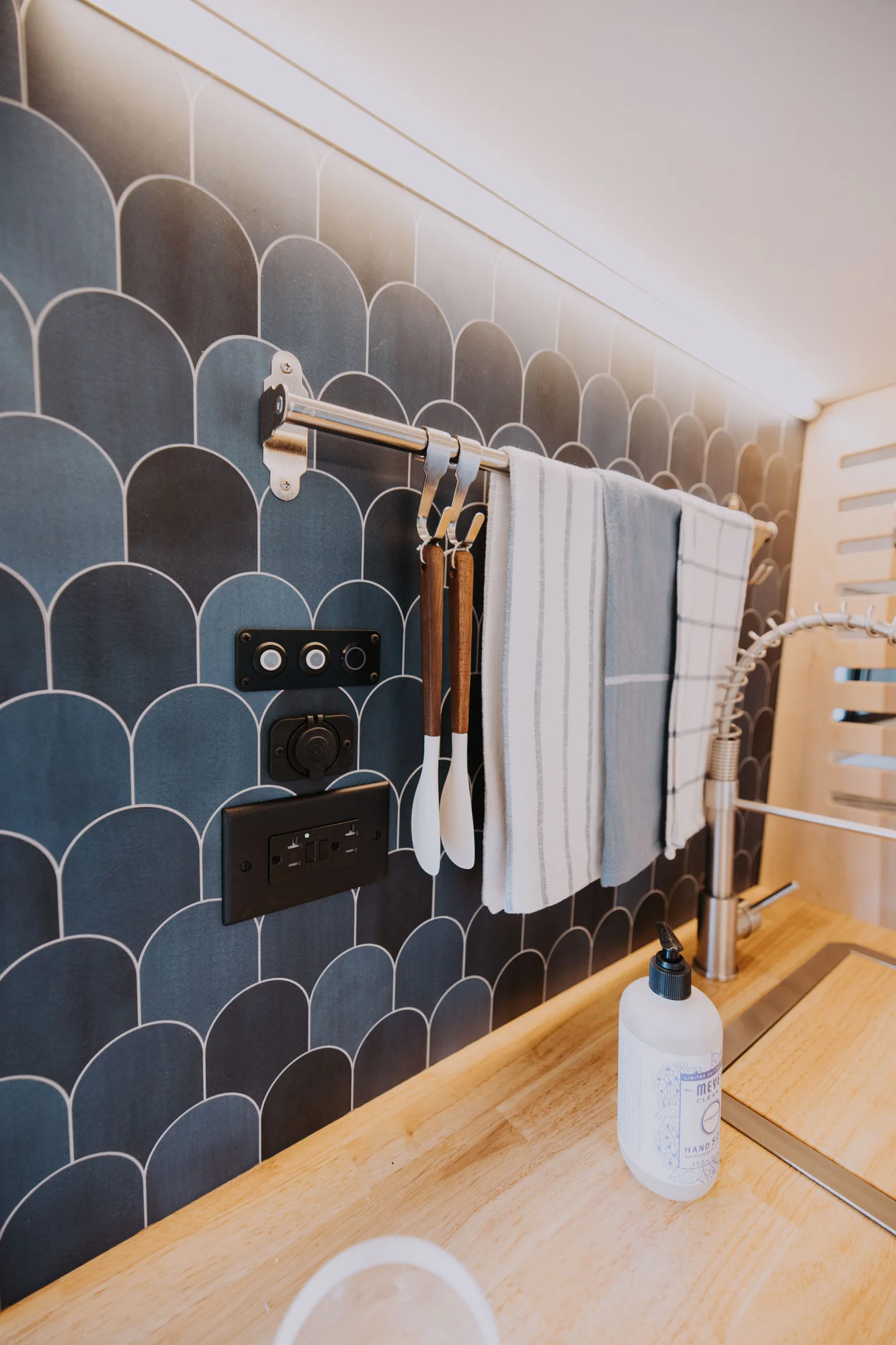 The Drifter 101 custom Ford Transit campervan built for Ayala by Drifter Vans, Drifter layout with warm wood cabinetry, a blue backsplash, flip-down shower, and an Avalanche Grey exterior