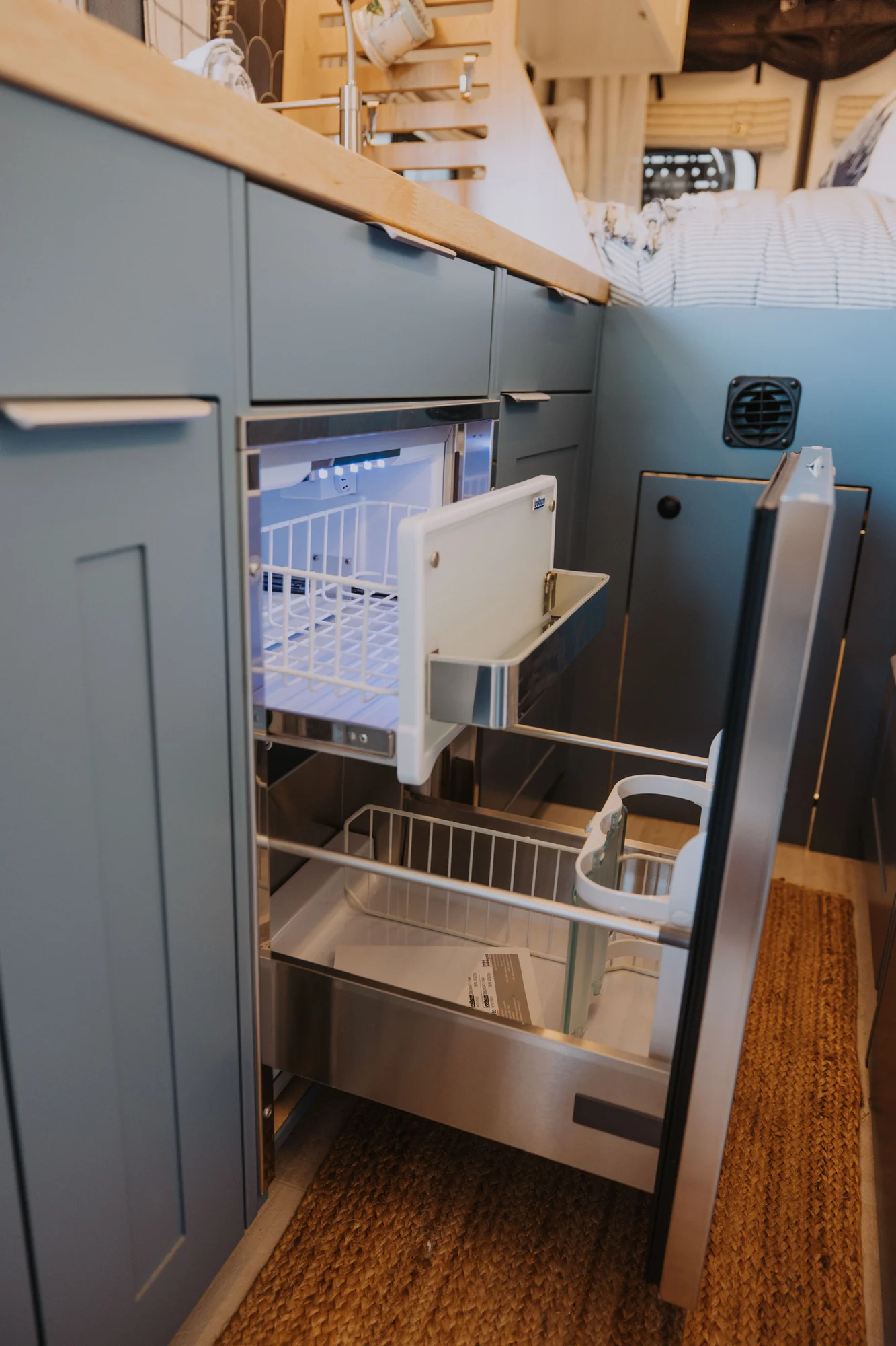 The Drifter 101 custom Ford Transit campervan built for Ayala by Drifter Vans, Drifter layout with warm wood cabinetry, a blue backsplash, flip-down shower, and an Avalanche Grey exterior