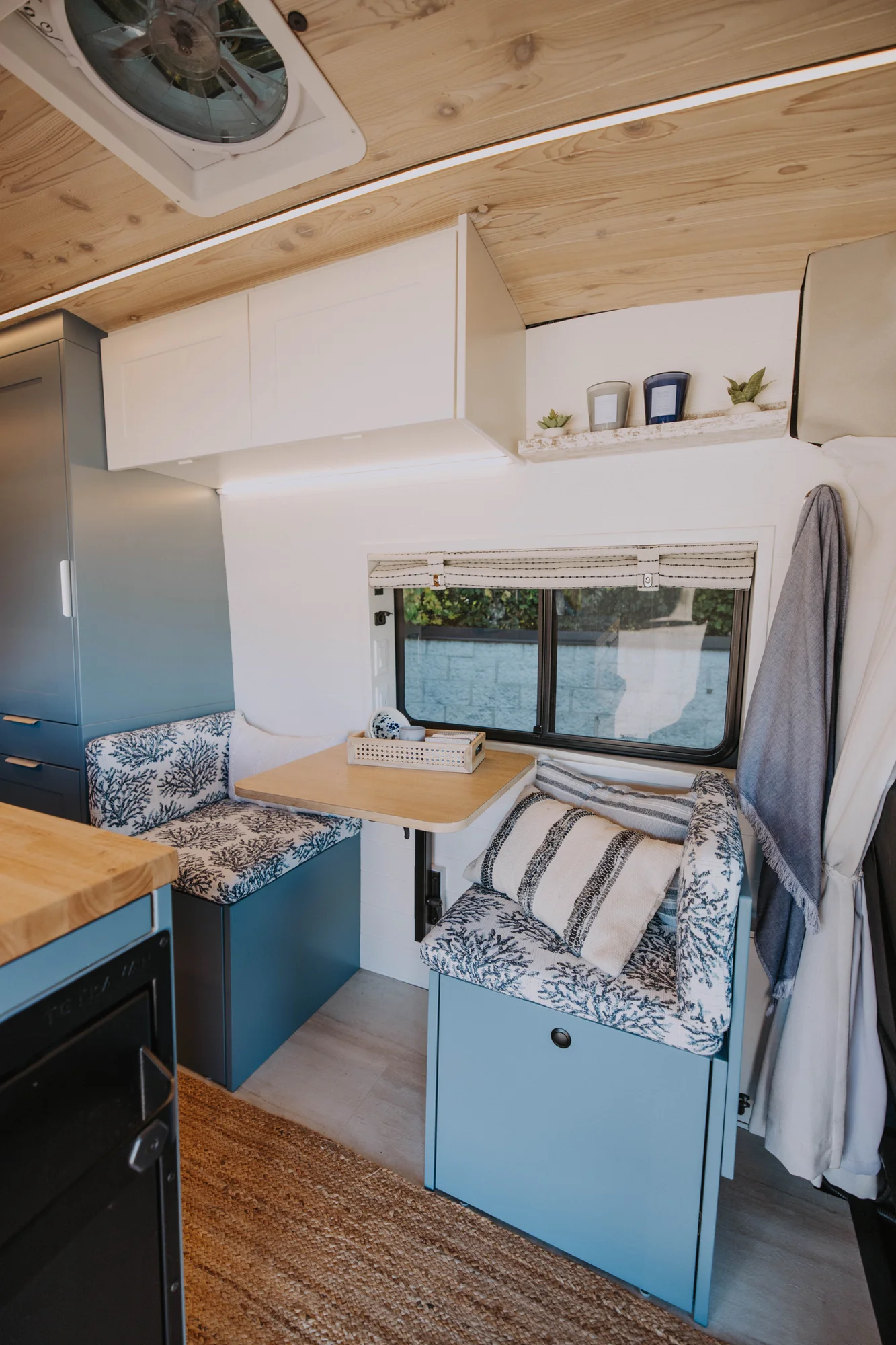 The Drifter 101 custom Ford Transit campervan built for Ayala by Drifter Vans, Drifter layout with warm wood cabinetry, a blue backsplash, flip-down shower, and an Avalanche Grey exterior