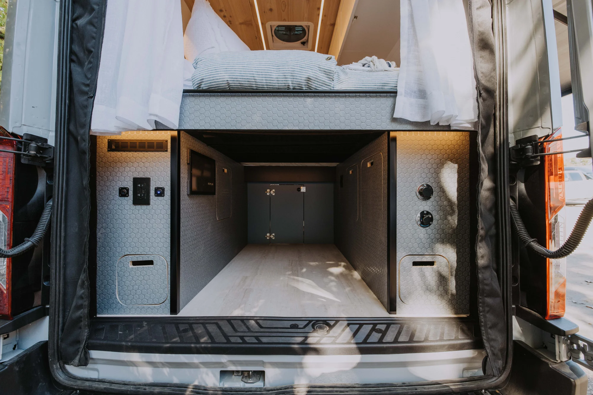 The Drifter 101 custom Ford Transit campervan built for Ayala by Drifter Vans, Drifter layout with warm wood cabinetry, a blue backsplash, flip-down shower, and an Avalanche Grey exterior