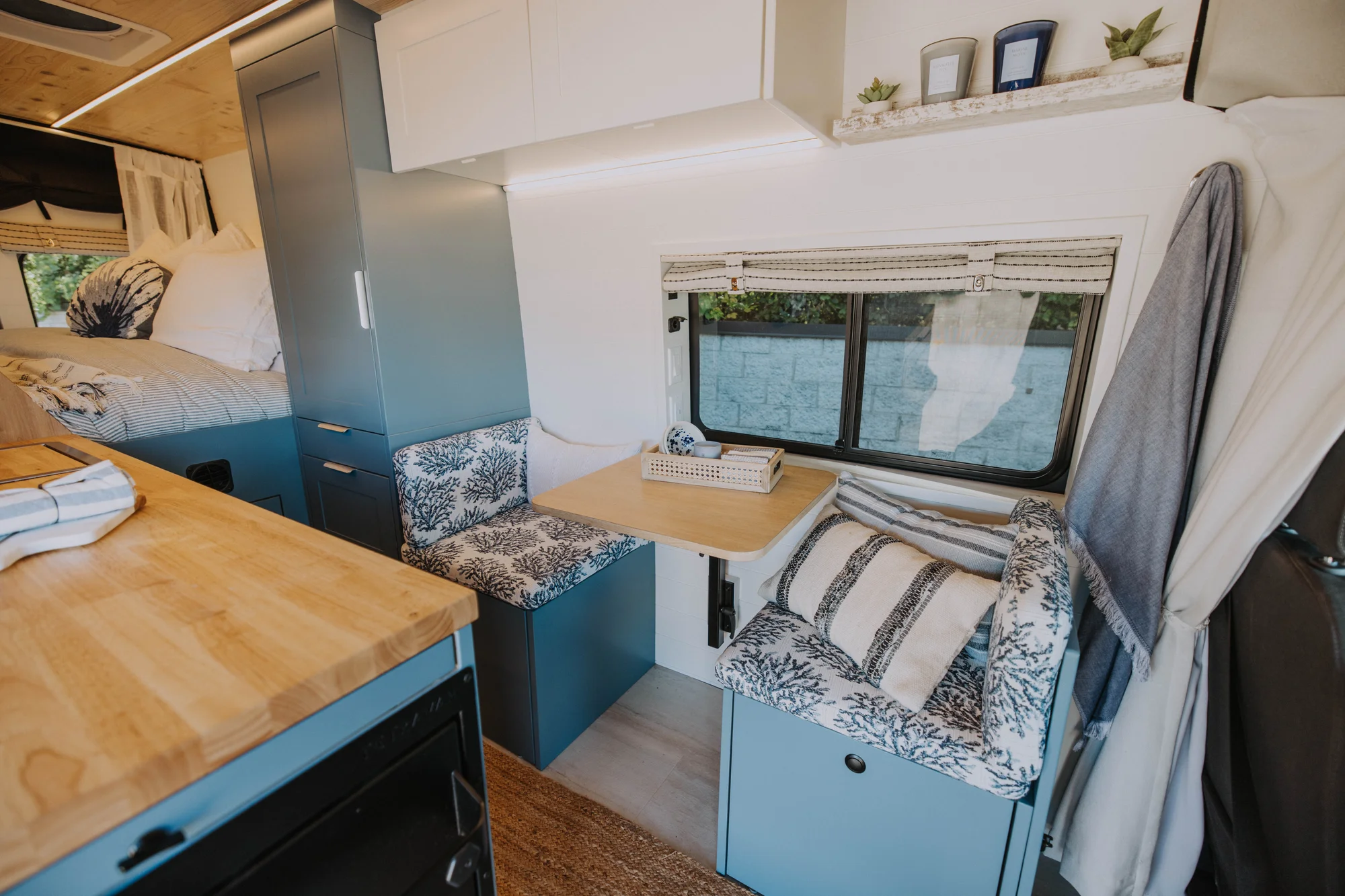 The Drifter 101 custom Ford Transit campervan built for Ayala by Drifter Vans, Drifter layout with warm wood cabinetry, a blue backsplash, flip-down shower, and an Avalanche Grey exterior