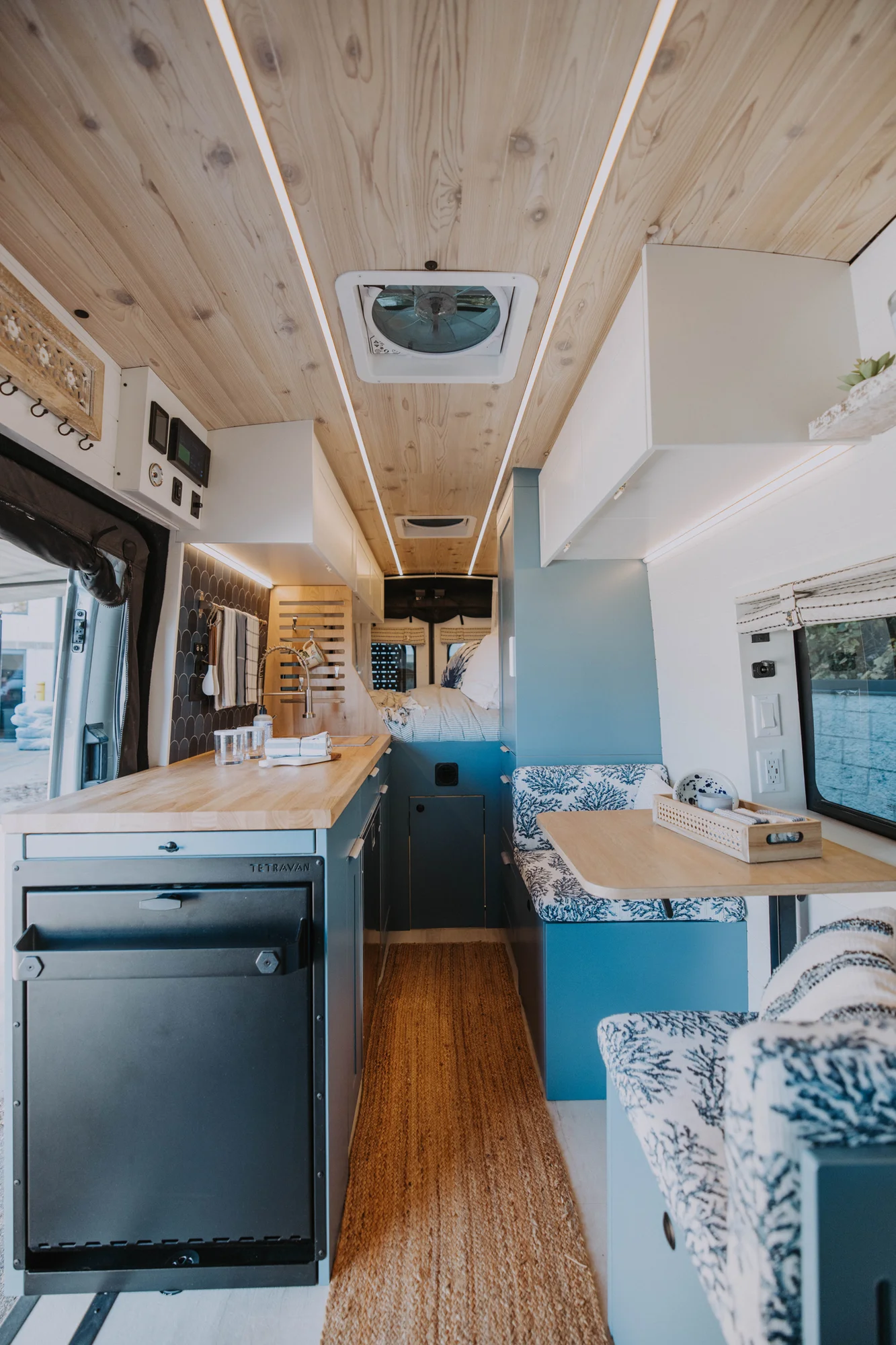 The Drifter 101 custom Ford Transit campervan built for Ayala by Drifter Vans, Drifter layout with warm wood cabinetry, a blue backsplash, flip-down shower, and an Avalanche Grey exterior