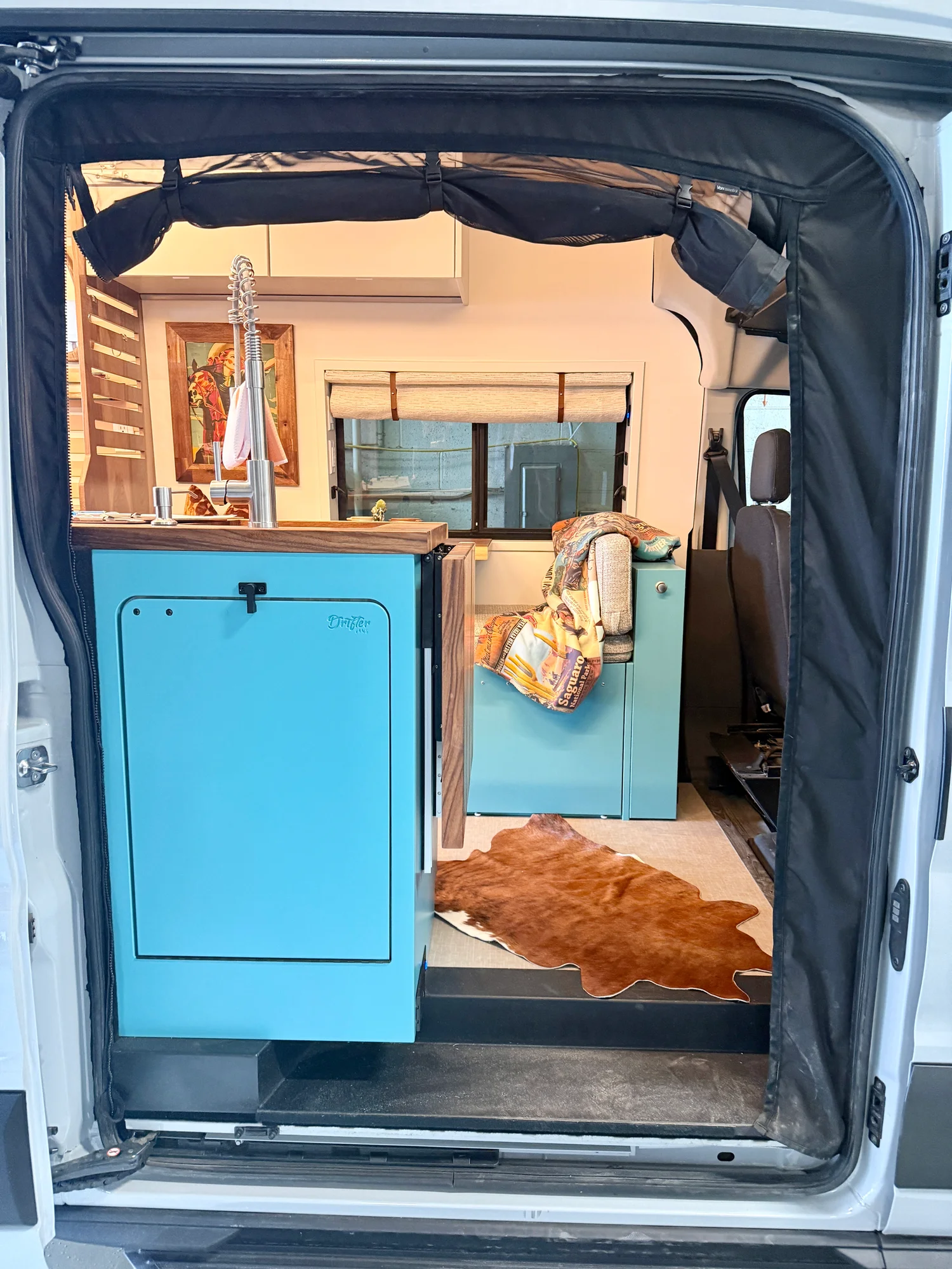 The Drifter 101 custom Ford Transit campervan built for Zach and Stephanie by Drifter Vans, with turquoise cabinetry, a custom wine rack, and Texas-inspired mid-century details
