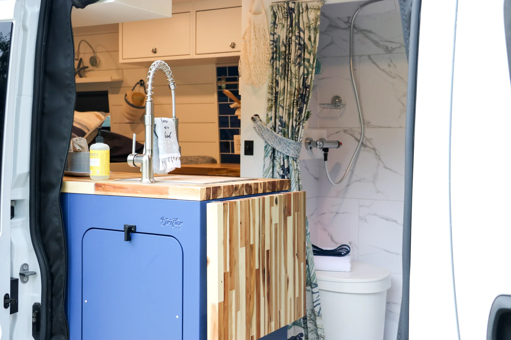 The Drifter 101 custom Ram ProMaster campervan built for Karen by Drifter Vans, Nomadik layout with coastal blue cabinetry, subway tile backsplash, and a white marble wet bath