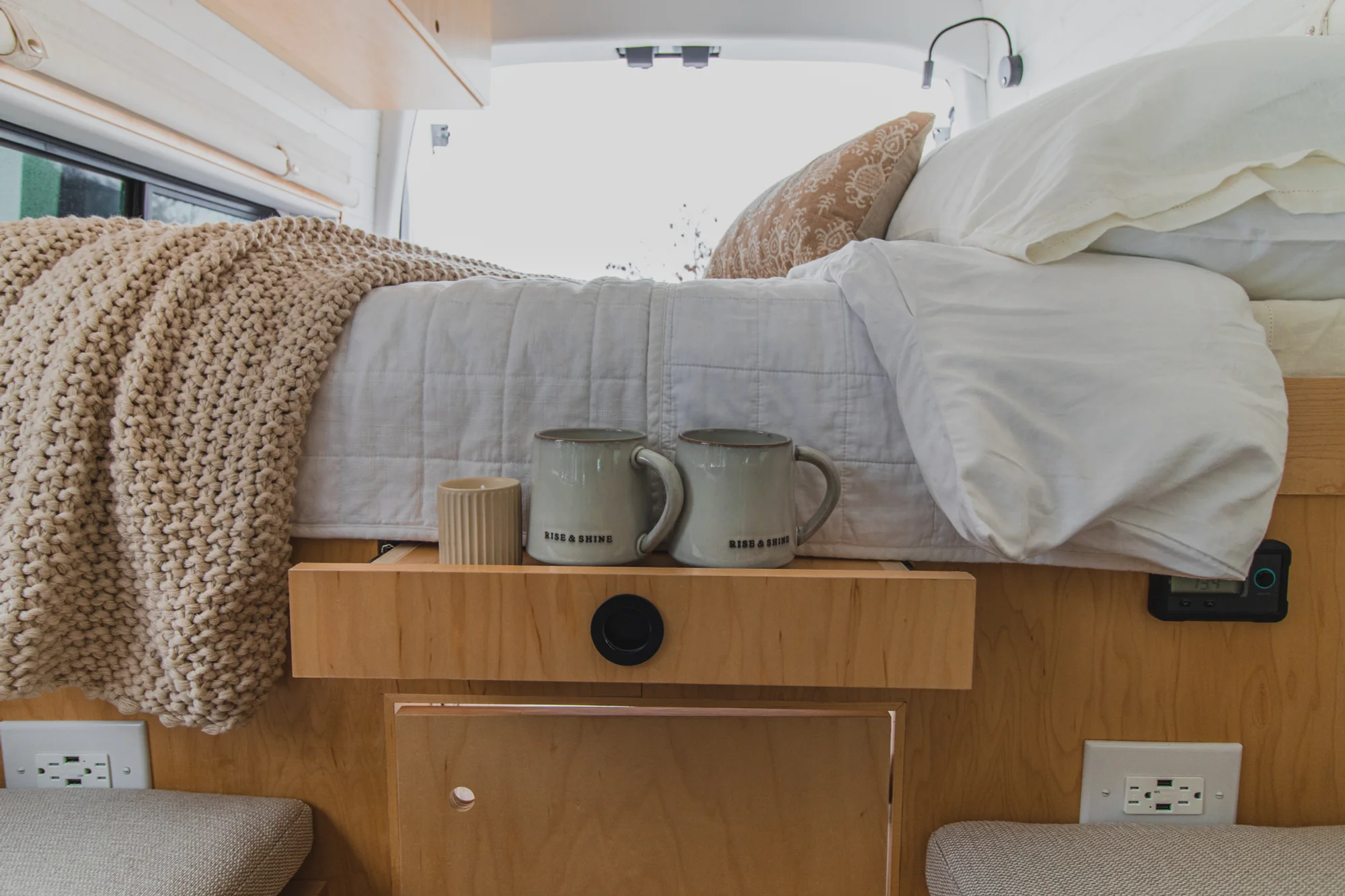 The Drifter 101 custom Ford Transit campervan built for Zach and Jacqueline by Drifter Vans, with a matte black sink and faucet, light wood cabinetry, and a raised bed with overhead shelves