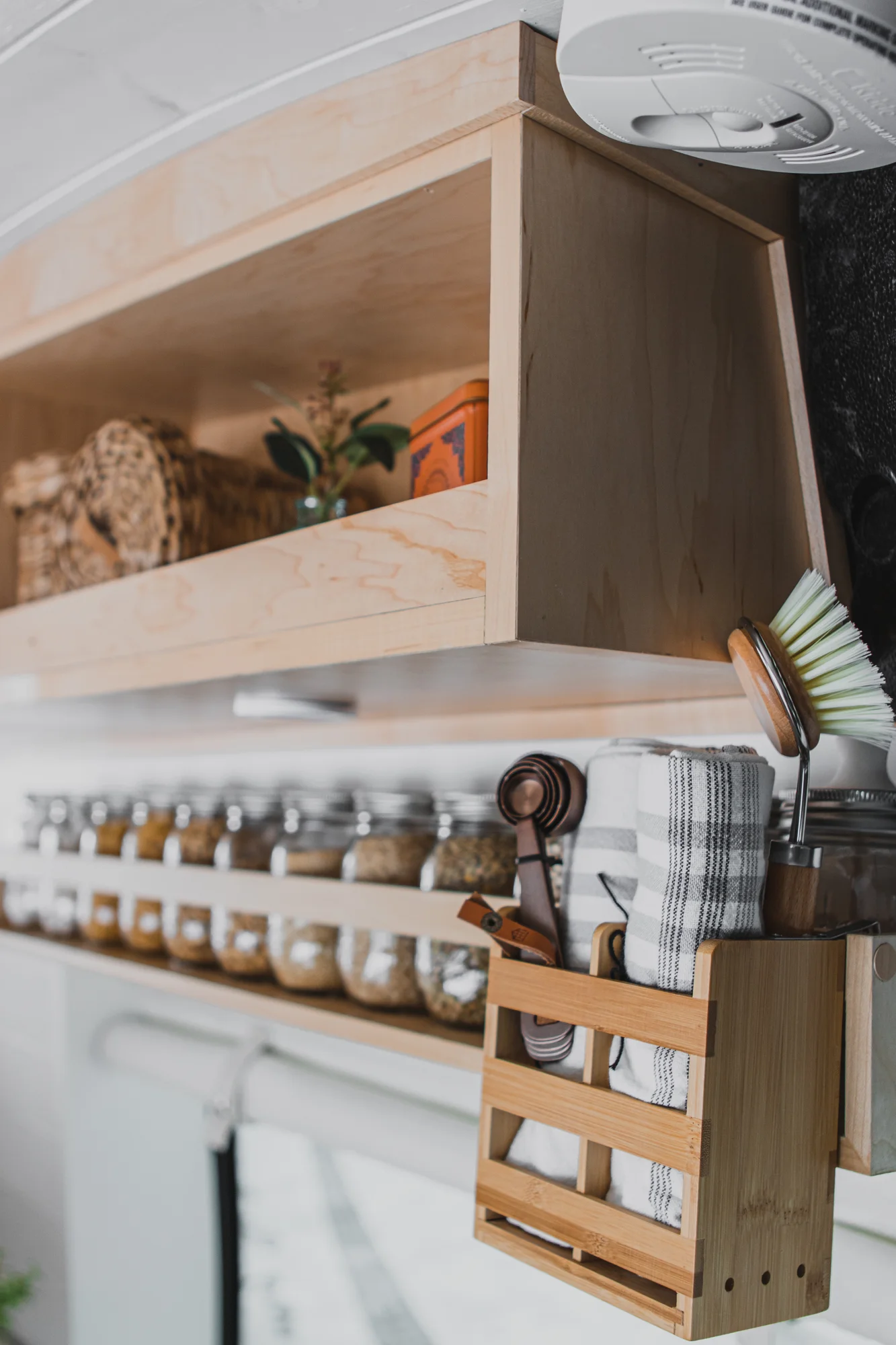 The Drifter 101 custom Ford Transit campervan built for Zach and Jacqueline by Drifter Vans, with a matte black sink and faucet, light wood cabinetry, and a raised bed with overhead shelves