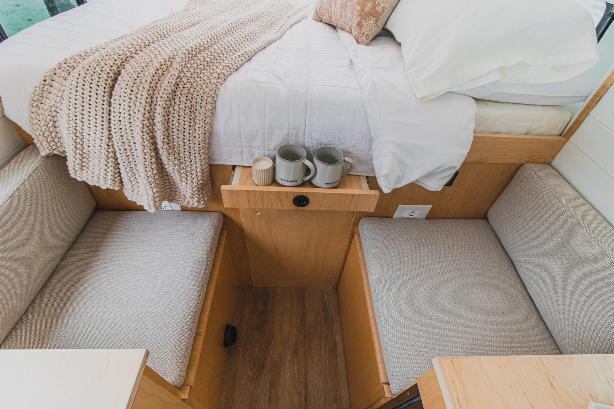 The Drifter 101 custom Ford Transit campervan built for Zach and Jacqueline by Drifter Vans, with a matte black sink and faucet, light wood cabinetry, and a raised bed with overhead shelves