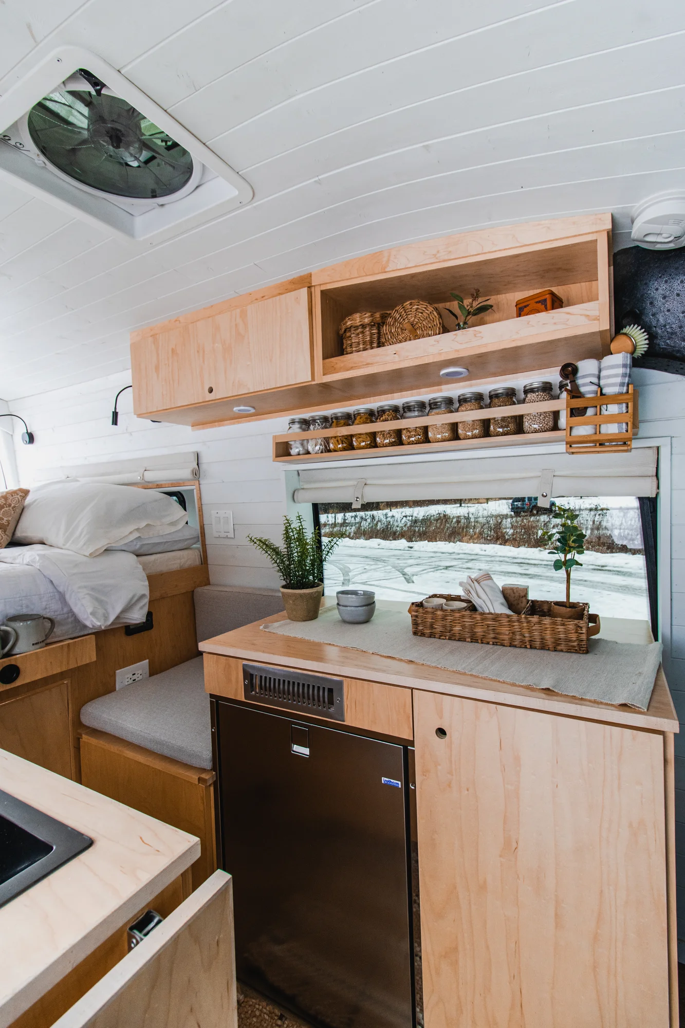 The Drifter 101 custom Ford Transit campervan built for Zach and Jacqueline by Drifter Vans, with a matte black sink and faucet, light wood cabinetry, and a raised bed with overhead shelves
