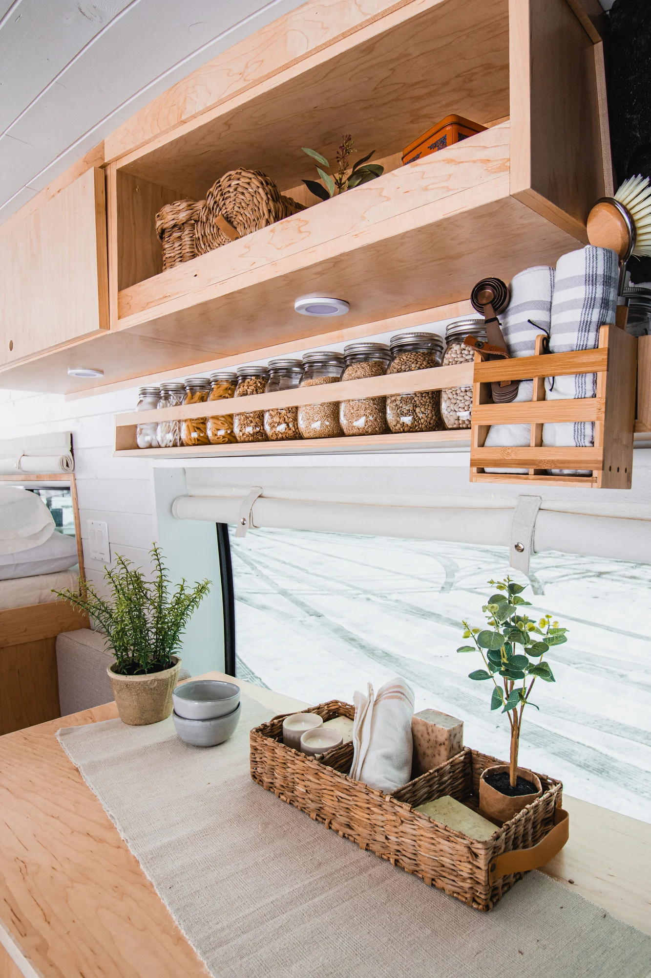 The Drifter 101 custom Ford Transit campervan built for Zach and Jacqueline by Drifter Vans, with a matte black sink and faucet, light wood cabinetry, and a raised bed with overhead shelves