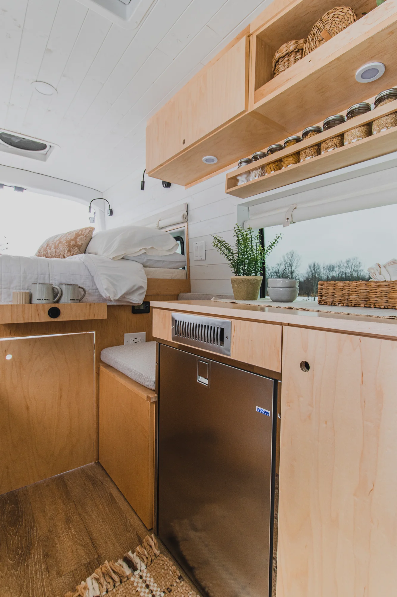 The Drifter 101 custom Ford Transit campervan built for Zach and Jacqueline by Drifter Vans, with a matte black sink and faucet, light wood cabinetry, and a raised bed with overhead shelves