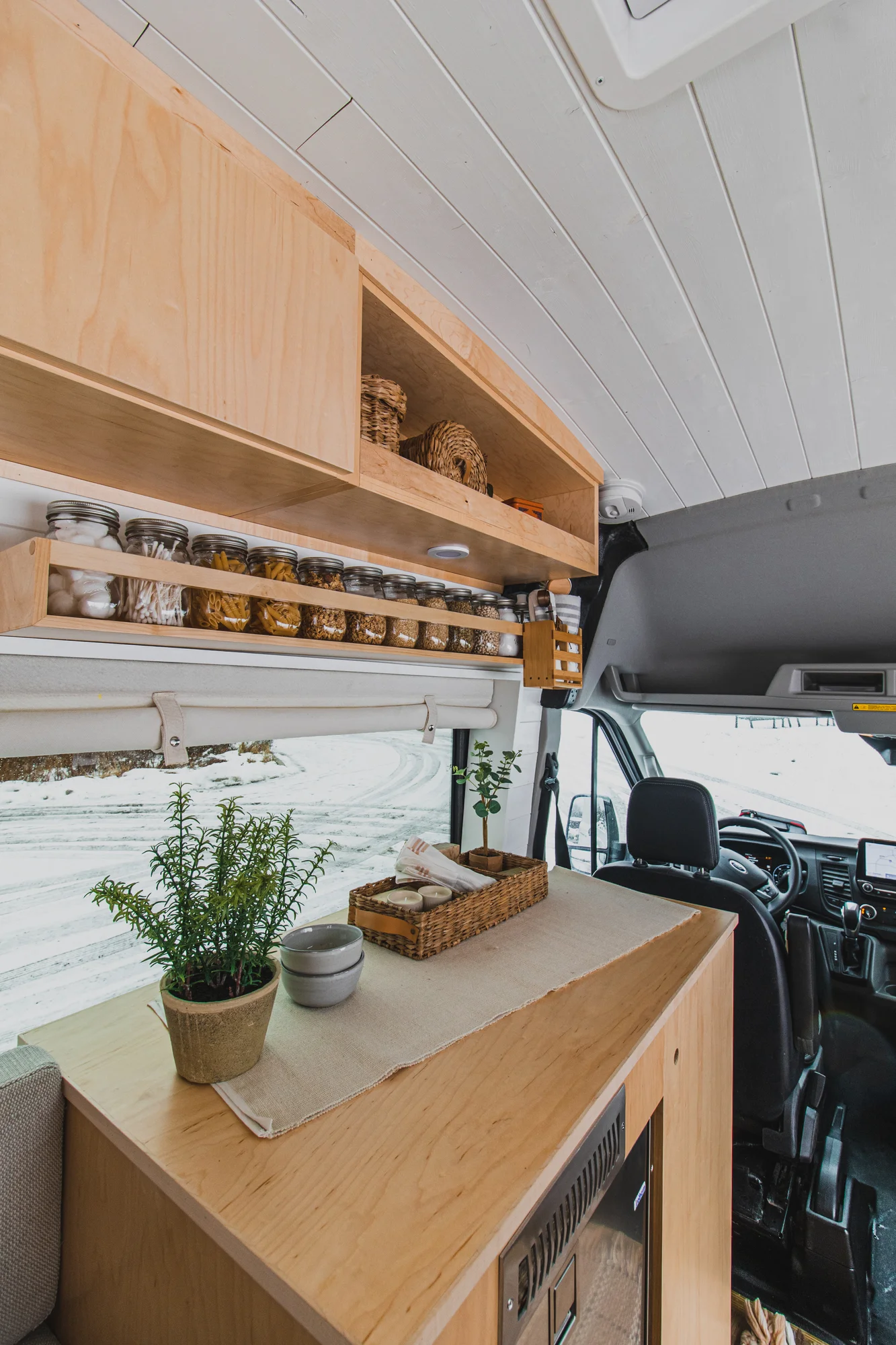 The Drifter 101 custom Ford Transit campervan built for Zach and Jacqueline by Drifter Vans, with a matte black sink and faucet, light wood cabinetry, and a raised bed with overhead shelves