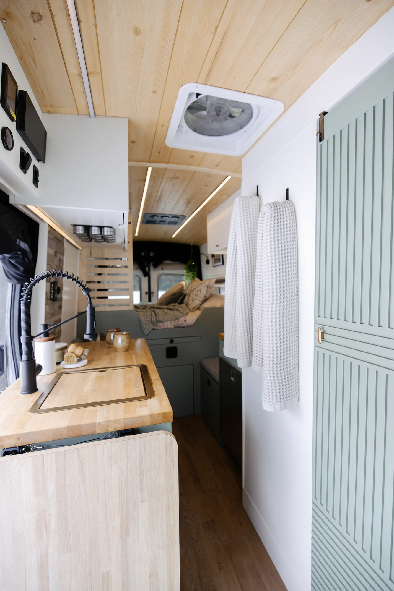 The Drifter 101 custom Ford Transit campervan built for Adrianne by Drifter Vans, Nomadik layout with knotty pine accents, soft green cabinetry, and a gold rain shower