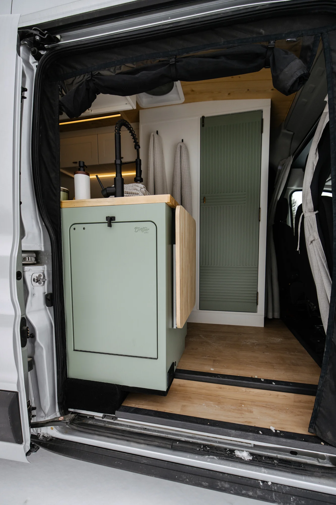 The Drifter 101 custom Ford Transit campervan built for Adrianne by Drifter Vans, Nomadik layout with knotty pine accents, soft green cabinetry, and a gold rain shower