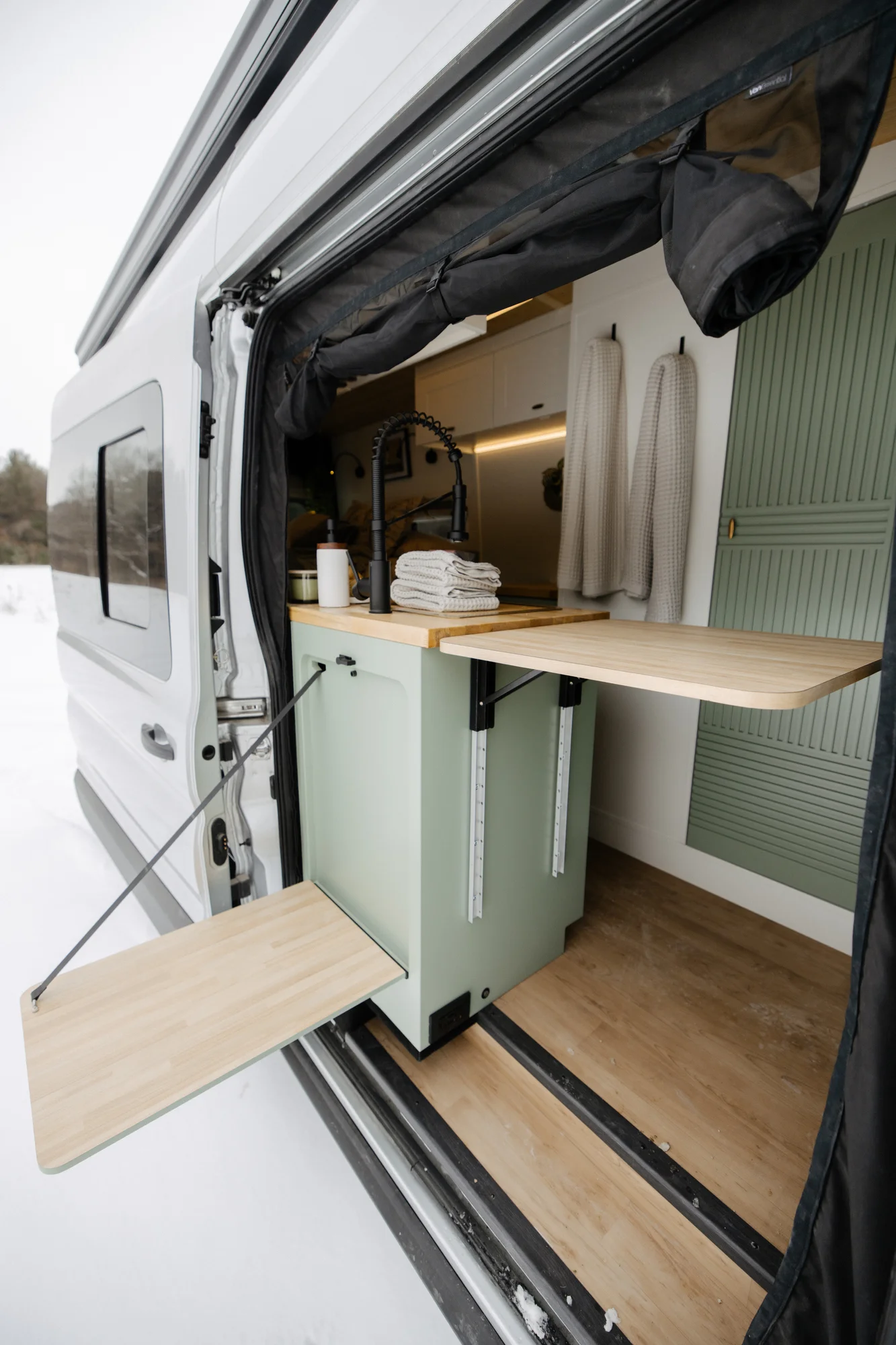 The Drifter 101 custom Ford Transit campervan built for Adrianne by Drifter Vans, Nomadik layout with knotty pine accents, soft green cabinetry, and a gold rain shower