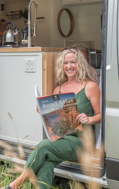Woman in hre 50's sitting on the edge of her drifter campervan reading an atlas