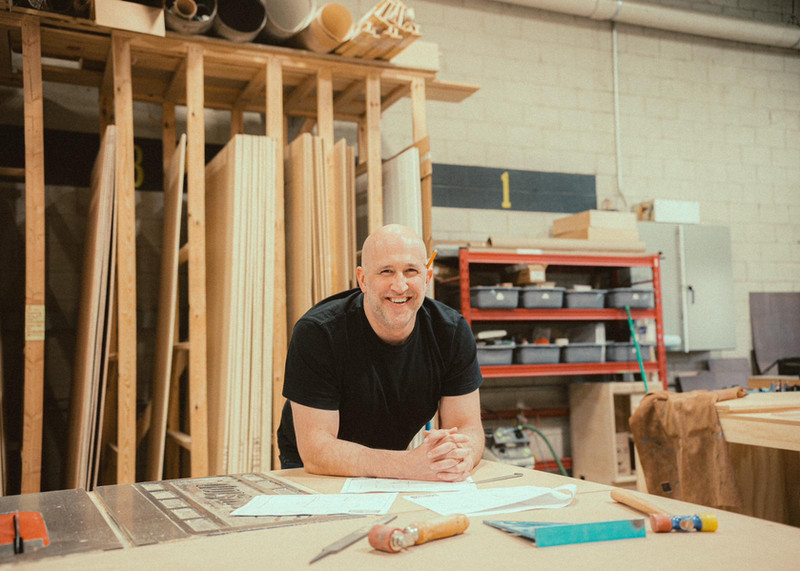 Paul Domish at the Drifter Vans workshop, leaning over a table saw while working on a custom van build component.