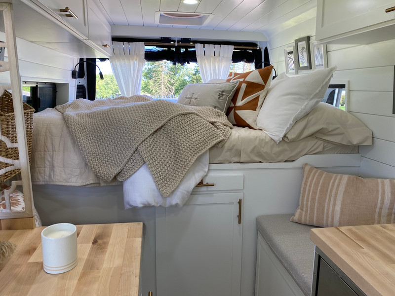 Beautiful interior of a camper van featuring a white boho finish with soft textures, natural wood accents, and a bright, airy design.