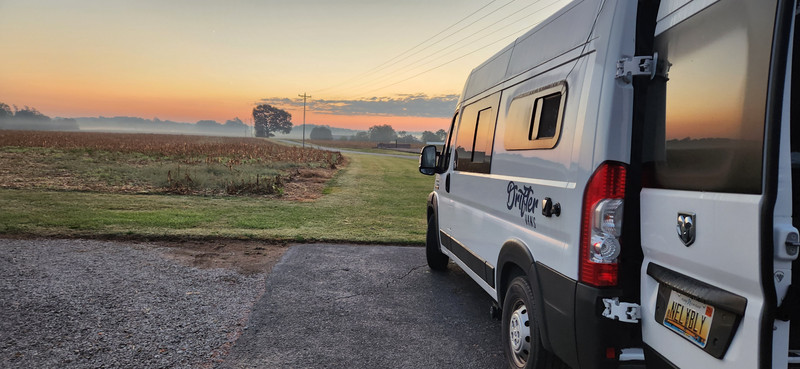 Susan’s Drifter Van parked against the backdrop of a stunning sunrise, with warm light illuminating the van and casting soft glows across the landscape.
