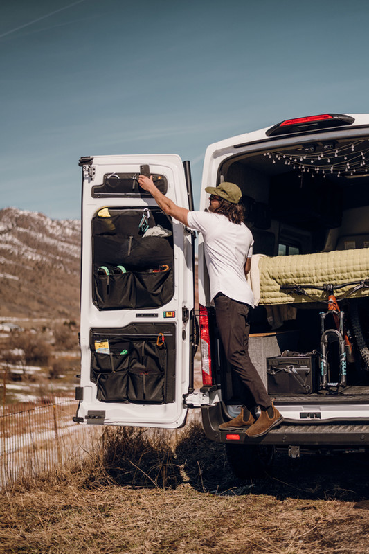 Man in the back of a ford transit campervan putting his stuff away in his van esential rear door storage bags