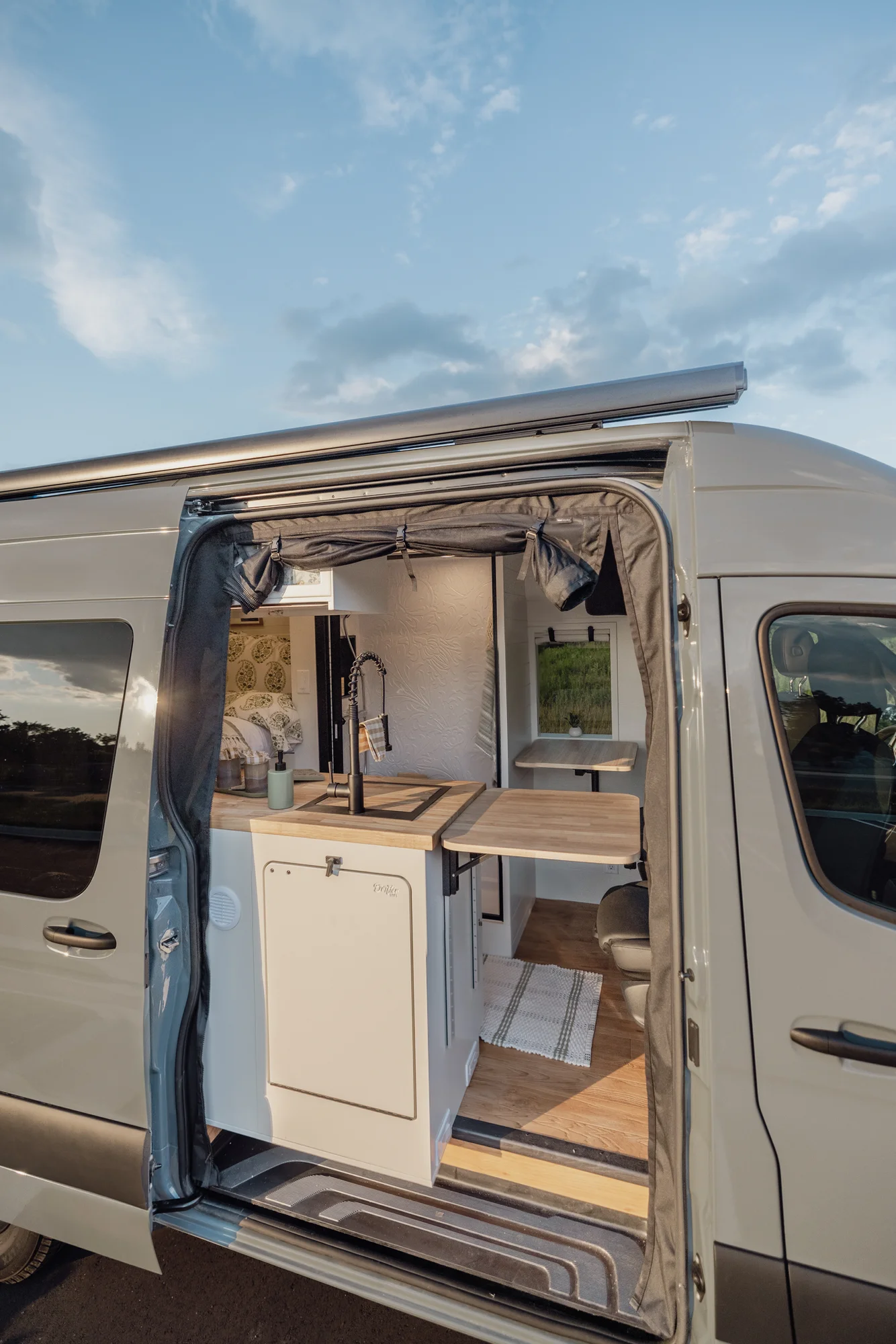 The Drifter 101 custom Mercedes-Benz Sprinter campervan built for Tanya by Drifter Vans, rustic interior with light blue cabinetry, butcher block countertop, and oil-rubbed bronze fixtures
