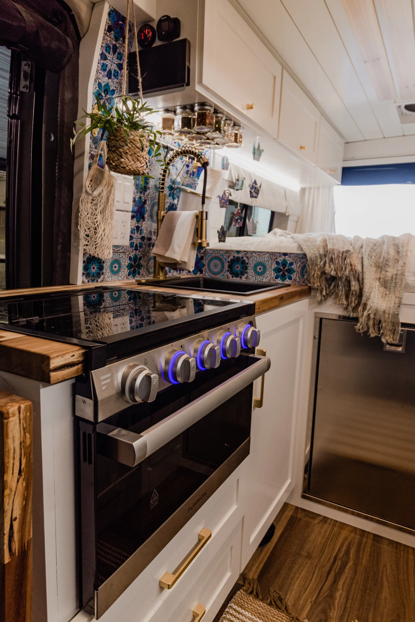 The Drifter 101 custom Ram ProMaster campervan built for Rhonda by Drifter Vans, Wanderer layout with a boho interior, Furrion oven, blue patterned tile backsplash, and brass hardware