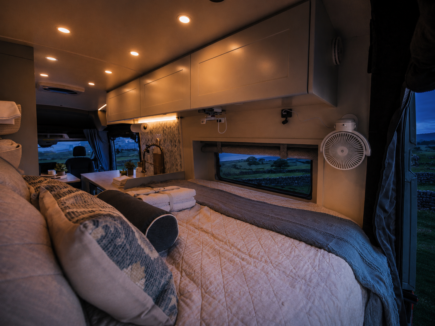 The Drifter 101 custom Ford Transit campervan built for Kathy by Drifter Vans, Drifter layout with Wedgewood Grey cabinetry, a Beige Travertine countertop, vintage brass faucet, and Charlotte Rattan cushions
