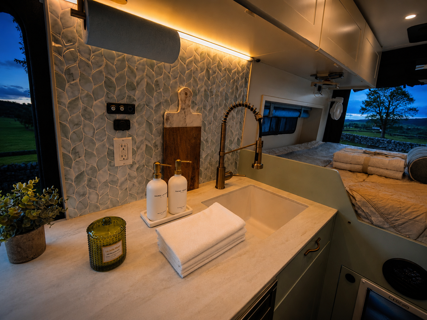 The Drifter 101 custom Ford Transit campervan built for Kathy by Drifter Vans, Drifter layout with Wedgewood Grey cabinetry, a Beige Travertine countertop, vintage brass faucet, and Charlotte Rattan cushions