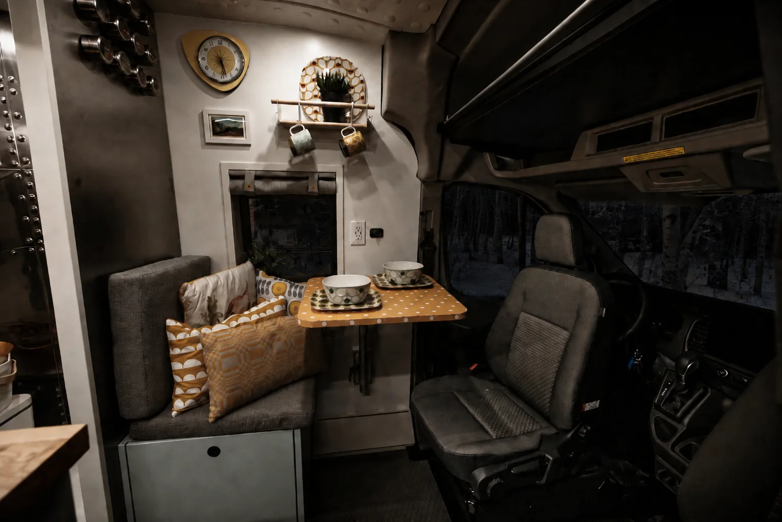 The Drifter 101 Ford Transit campervan built for Edward and Caroline by Drifter Vans: retro dinette with mustard polka-dot swivel table, patterned cushions and vintage wall clock beside the swiveled cab seat