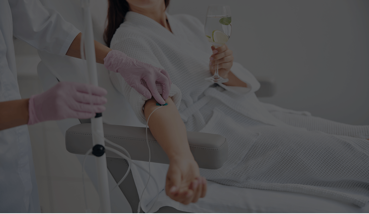 Patient in a white robe receiving intravenous therapy while holding a glass of water with lemon and mint.