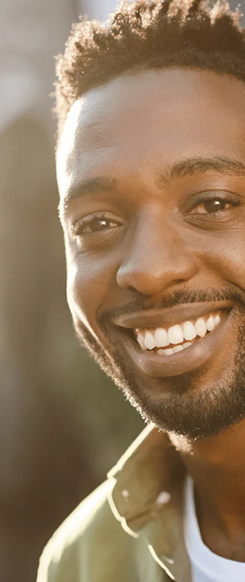 Man smiling warmly at the camera in sunlight, wearing a green shirt.