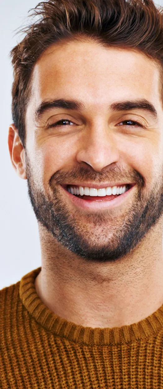 Smiling man with a beard, wearing a brown sweater, against a light background.