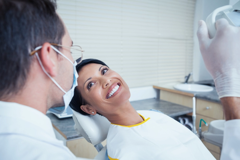 A dentist examines a smiling patient in the dental chair.