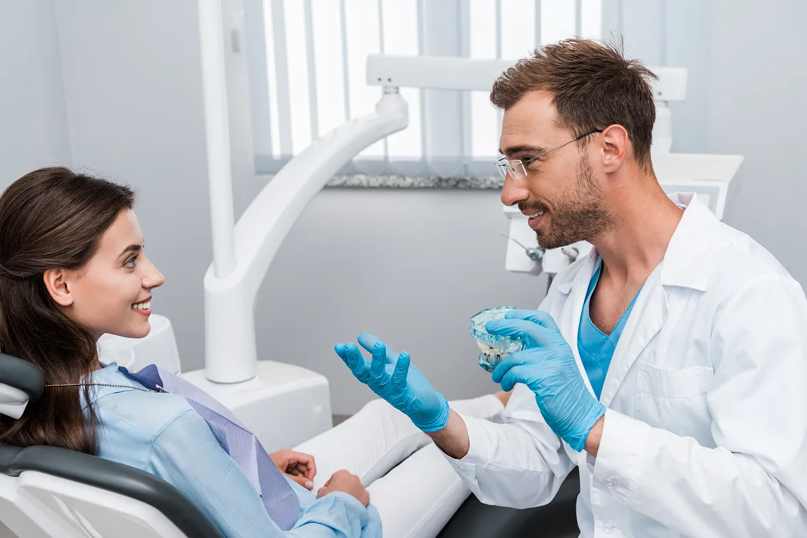 Dentist explaining a dental model to a smiling woman sitting in a dental chair.
