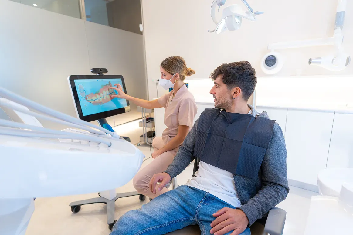 A dental professional shows a patient dental images on a screen in an examination room.