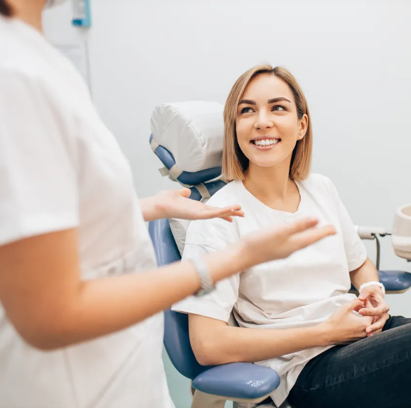 A woman sits in a dental chair, smiling and talking with a dental professional.