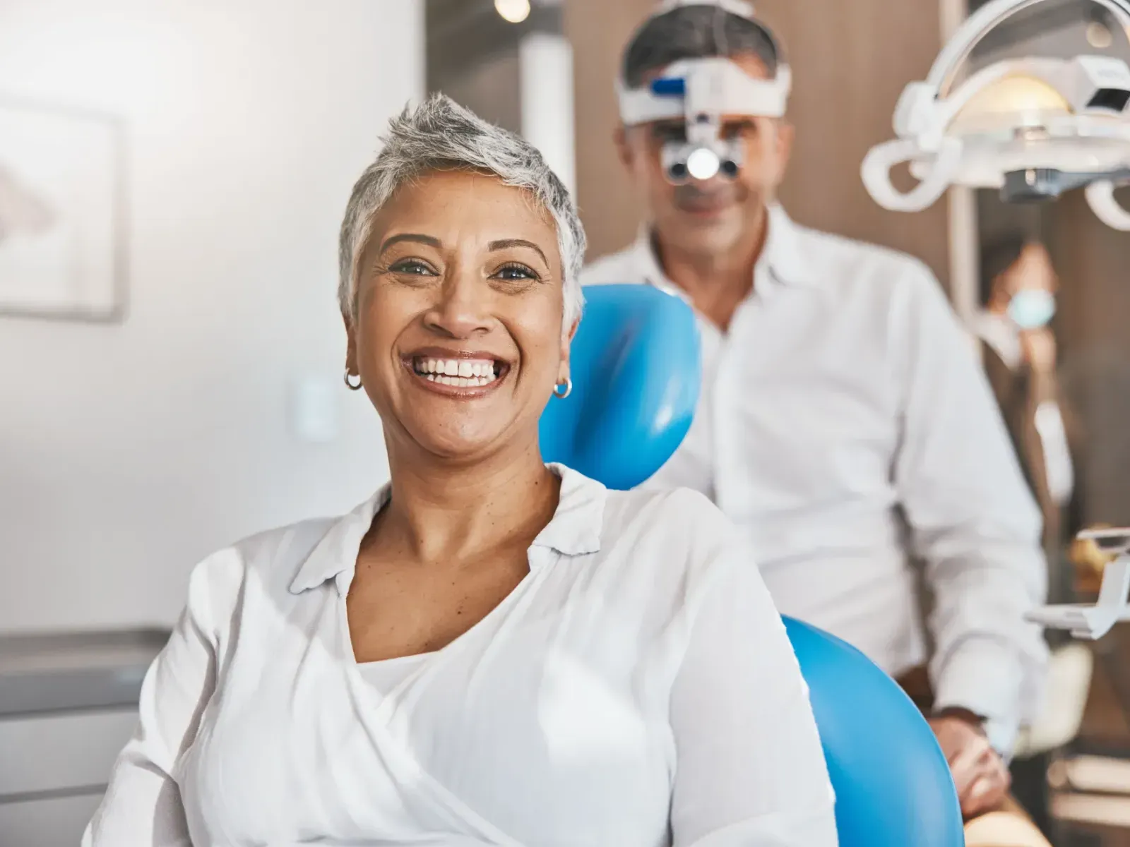 A woman smiles in a dental chair while a dentist stands behind her.