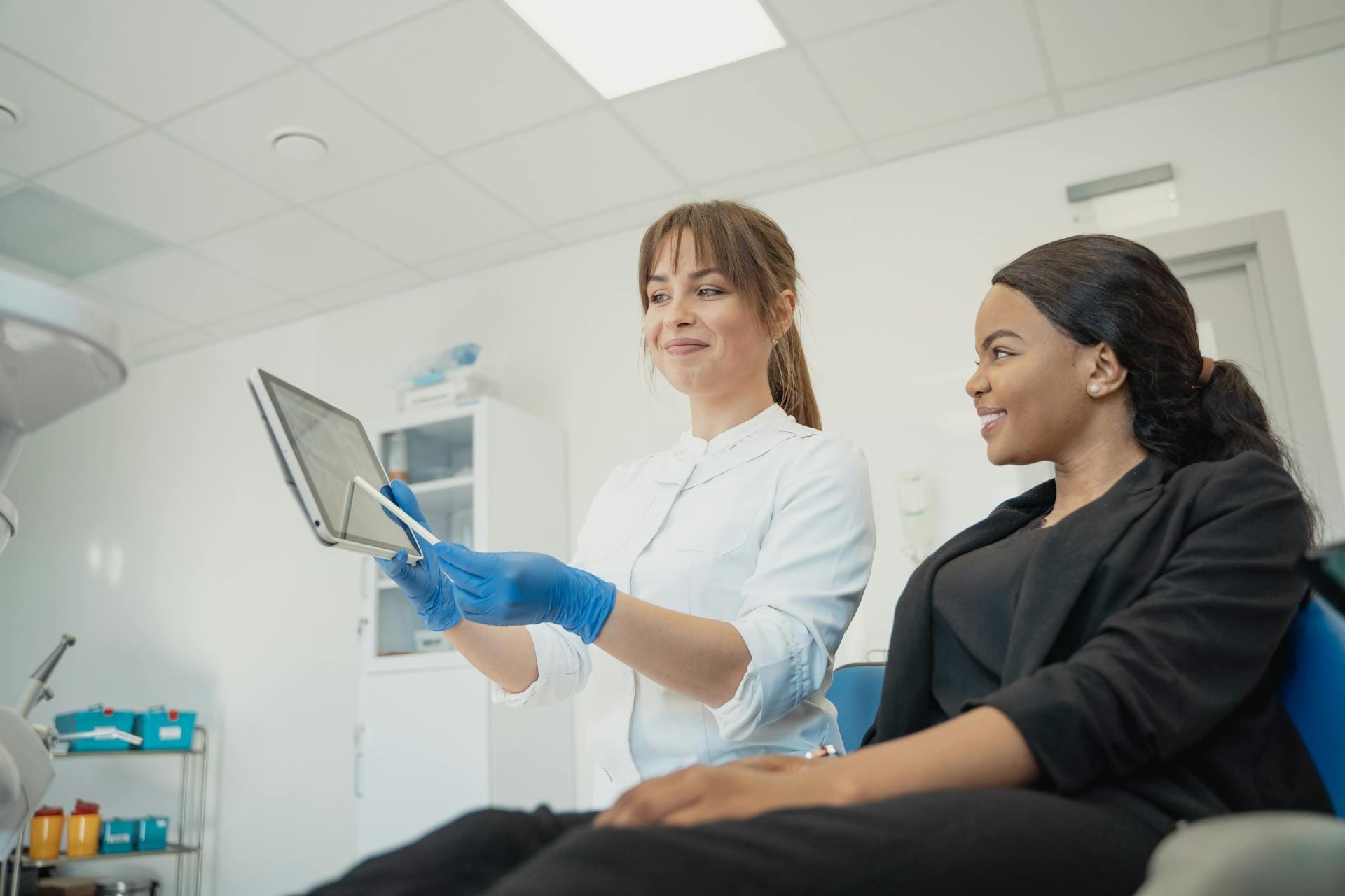A dental professional shows a tablet to a patient sitting in a dental chair.