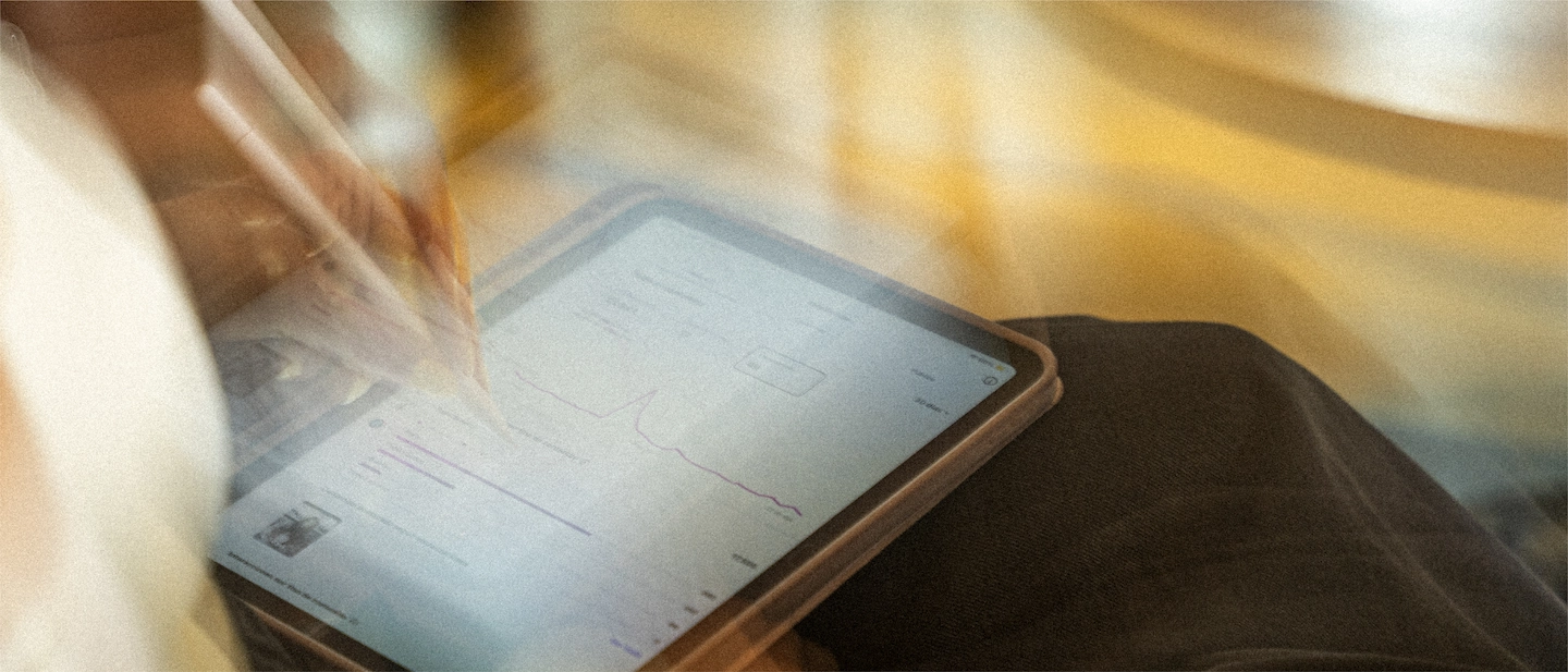Persona sostiene una tablet que muestra en pantalla un panel de métricas con gráficas de líneas, iluminada por luz cálida y con desenfoque de movimiento que sugiere un ambiente de trabajo dinámico enfocado en análisis de datos o desempeño de campañas.