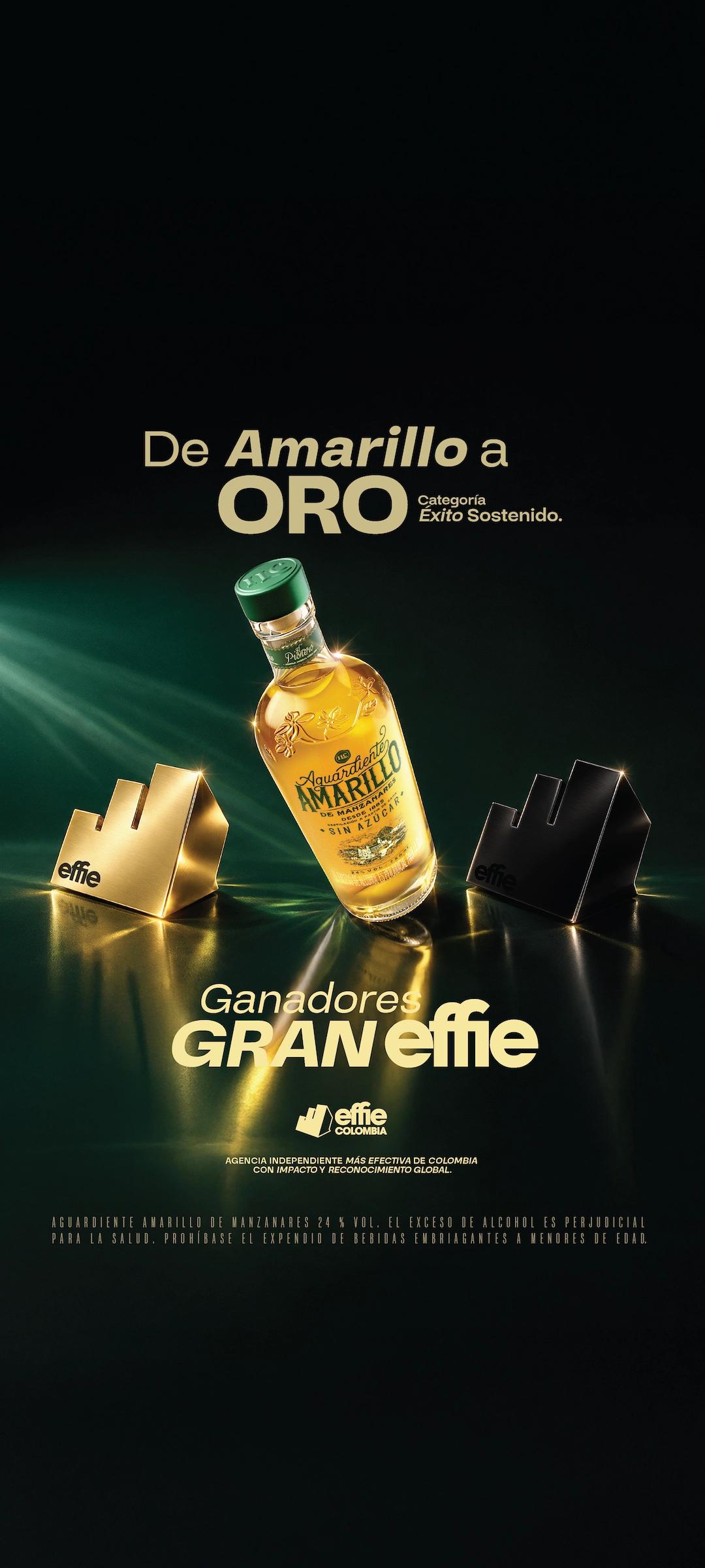 Botella de Aguardiente Amarillo junto a dos trofeos Effie, uno dorado y otro negro, con el texto De Amarillo a Oro Categoría Éxito Sostenido y Ganadores Gran Effie, destacando el premio Effie Colombia como agencia independiente más efectiva de Colombia con impacto y reconocimiento global.