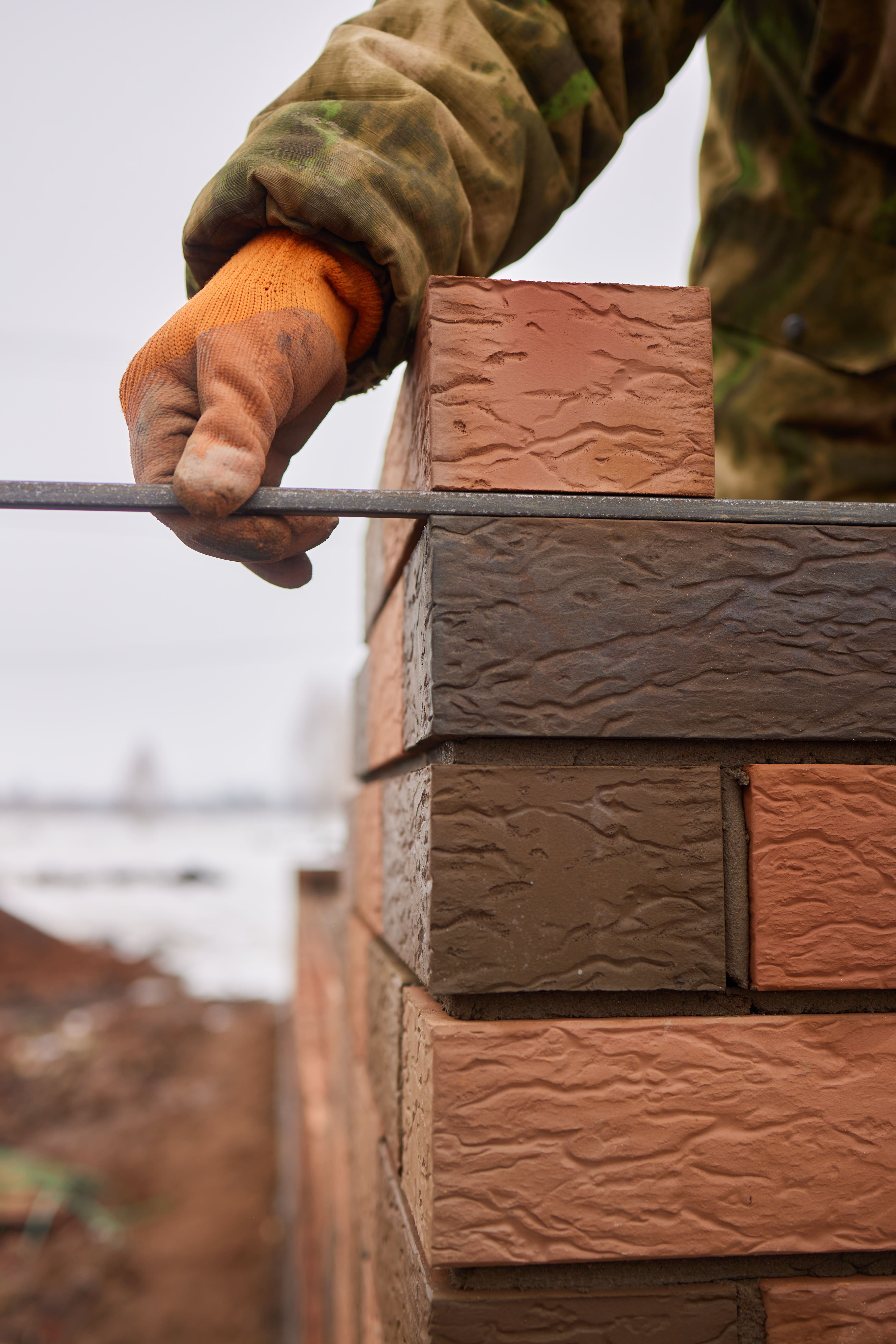Metselaar werkt de voegen van een bakstenen gevel strak af met een voegijzer tijdens de nieuwbouw van een woning.